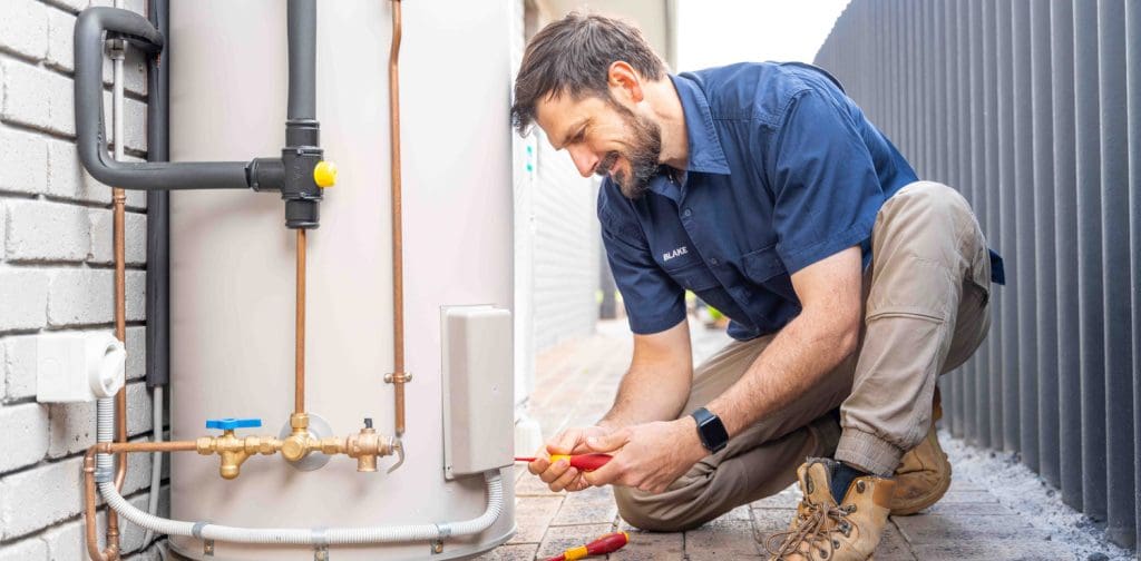Electrician performing maintenance on a water heater outside a building.