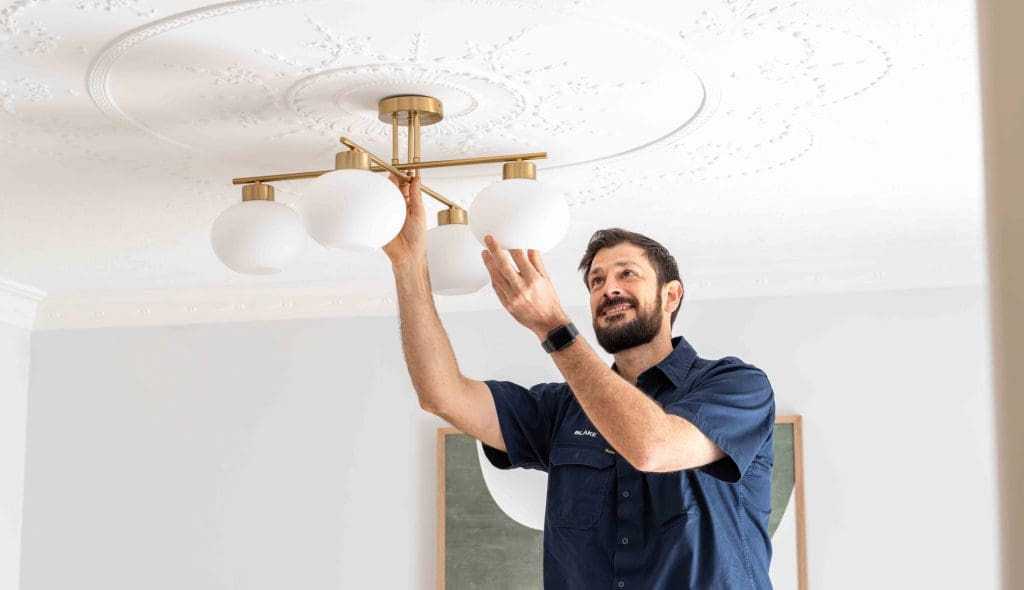 Electrician installing a modern ceiling light fixture in a room.