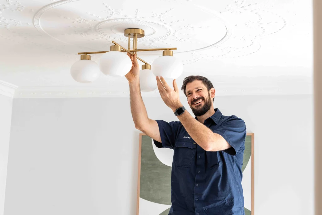 Electrician installing ceiling lights with a smile in a modern home setting.